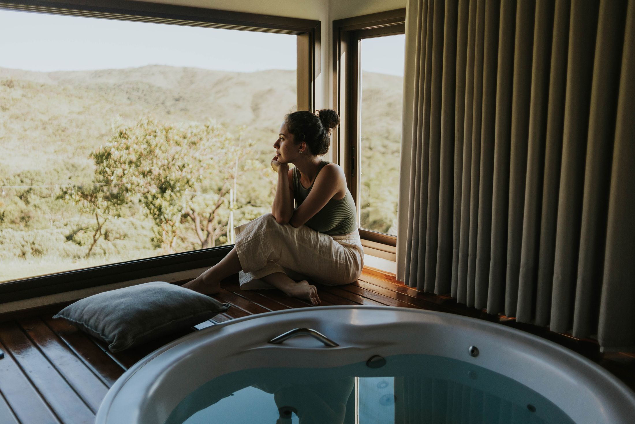 A person sitting by a window beside a round bath, looking out over hills. Illustrative stock photograph, not an Almajour property